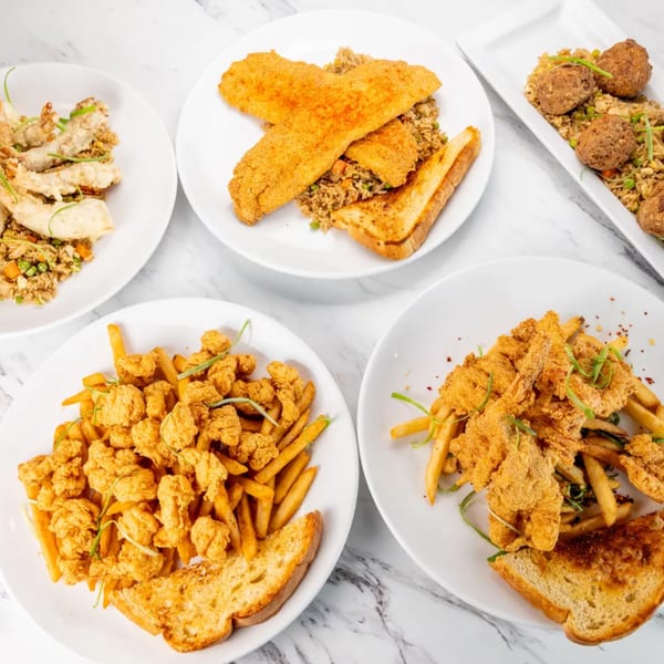 Four plates of fried seafood, including fish, shrimp, and hush puppies, with fries, rice, and toast.