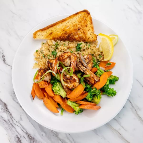 Grilled shrimp with rice, sautéed carrots, broccoli, and a slice of toasted bread on a white plate.