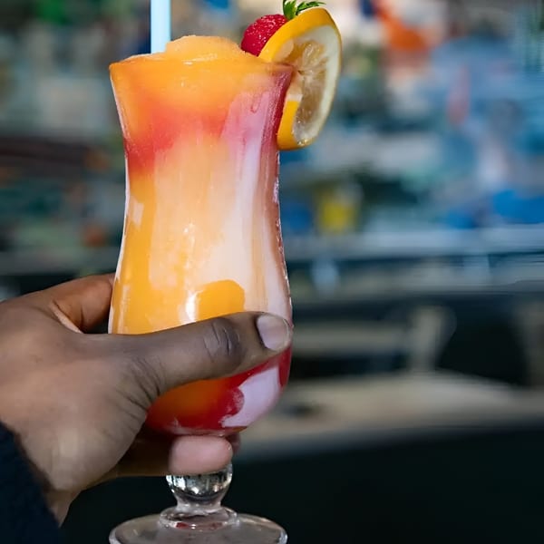 A hand holding a vibrant, layered frozen drink garnished with a strawberry and lemon slice.