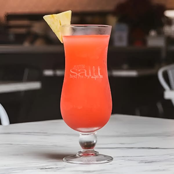 A vibrant red cocktail with a pineapple wedge garnish, served in a tall glass on a white table.