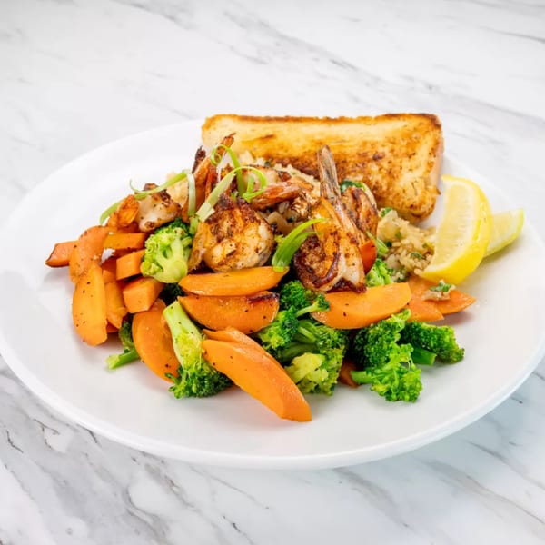 Grilled shrimp and vegetables with rice and garlic bread on a white plate.
