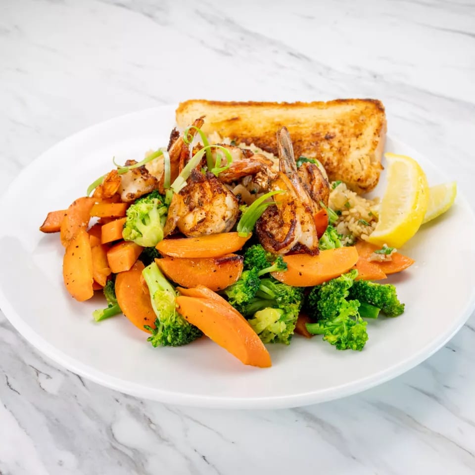 Grilled shrimp and vegetables with rice and garlic bread on a white plate.