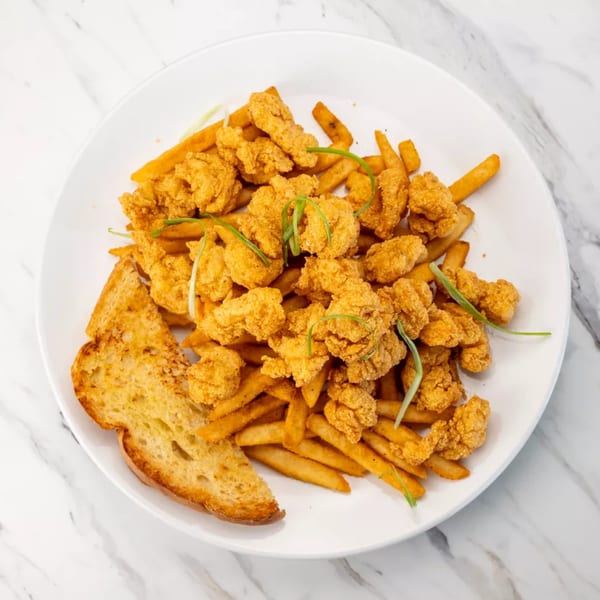 Crispy fried shrimp and french fries with a slice of garlic bread on a white plate.