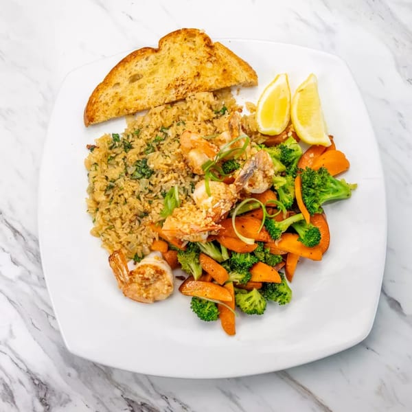Shrimp scampi with rice, roasted broccoli, carrots, and garlic bread on a white plate.