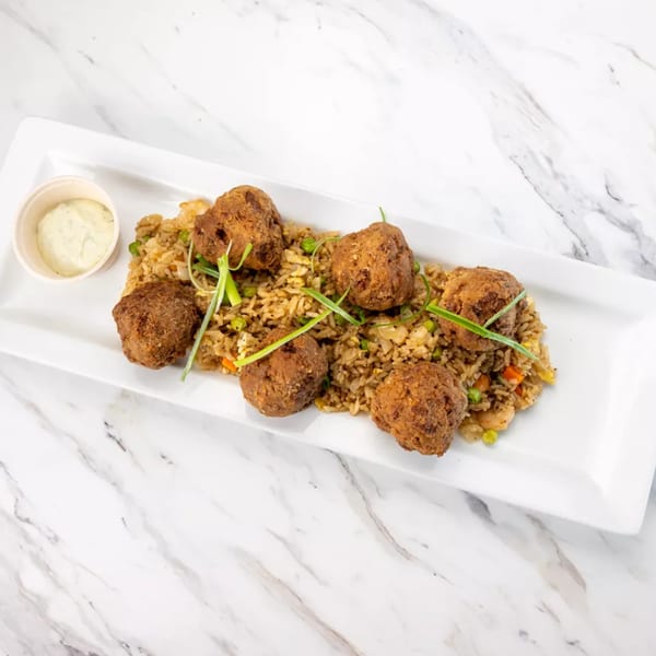 Fried rice with six brown, round fritters and a side of white dipping sauce on a white platter.