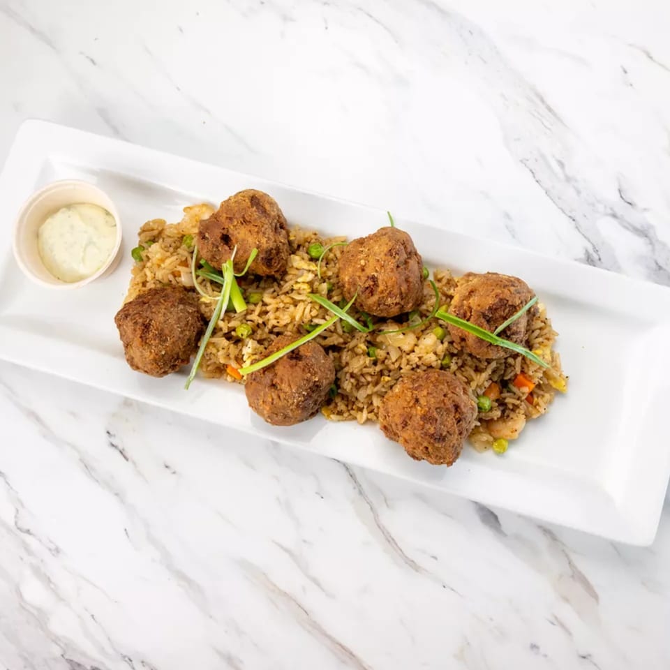 Fried rice with six brown, round fritters and a side of white dipping sauce on a white platter.