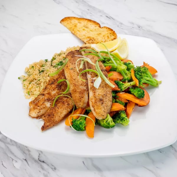 Seasoned fish fillets with rice, mixed vegetables, lemon wedges, and garlic bread on a white plate.