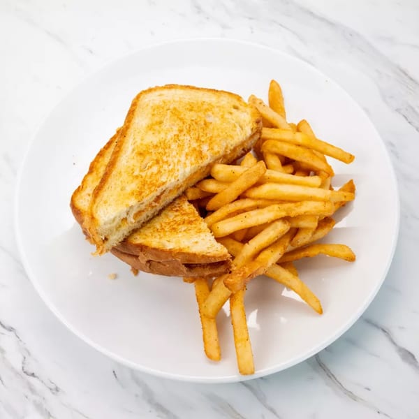 Grilled cheese sandwich cut in half, served with a side of golden french fries on a white plate.