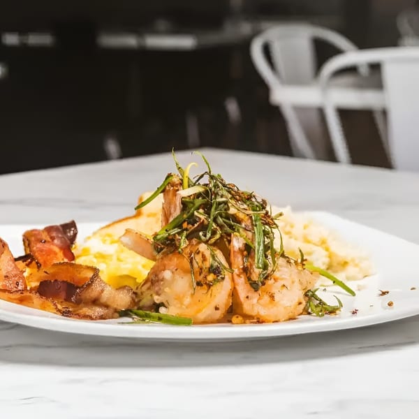 Shrimp and grits with bacon and herbs on a white plate, with a blurred background.