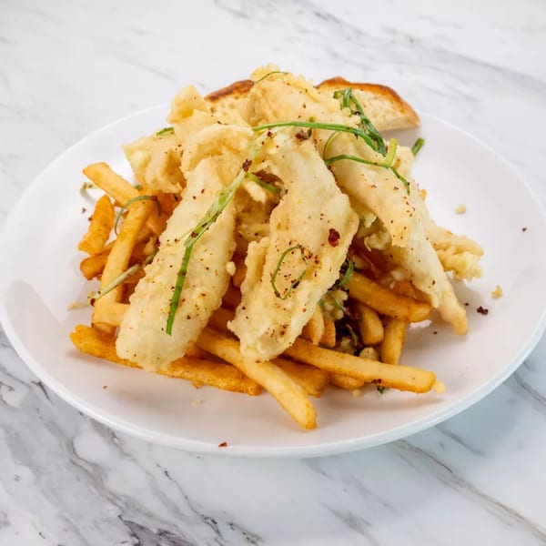 Crispy fried fish and golden french fries on a white plate, garnished with green herbs.