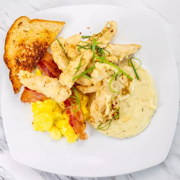 Fried chicken, grits, scrambled eggs, bacon, and toast on a white plate.