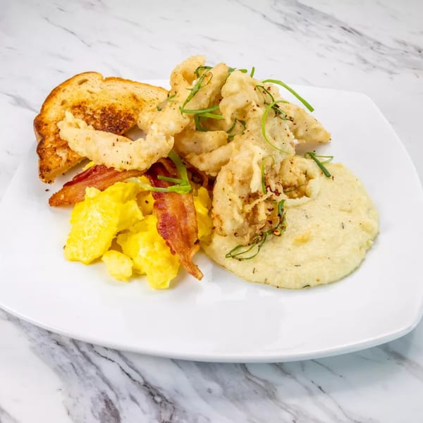 Fried calamari with grits, scrambled eggs, bacon, and toast on a white plate.