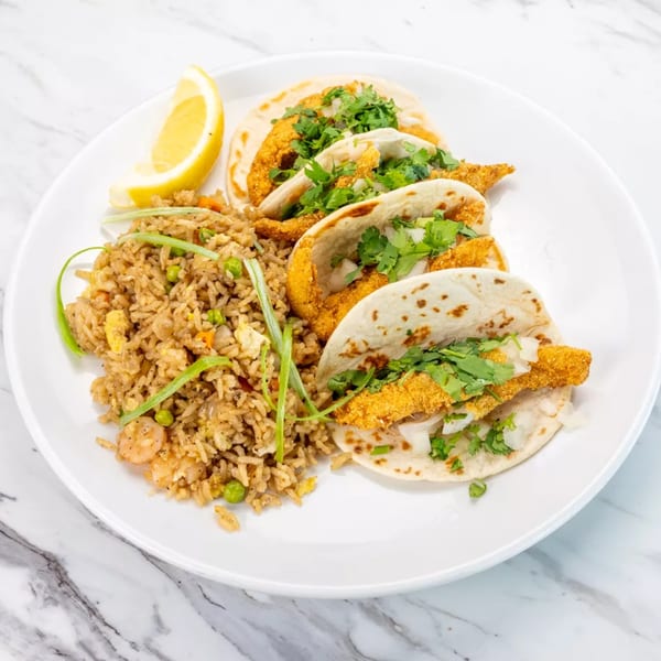 Three fish tacos with cilantro and onions, served with fried rice and a lemon wedge.