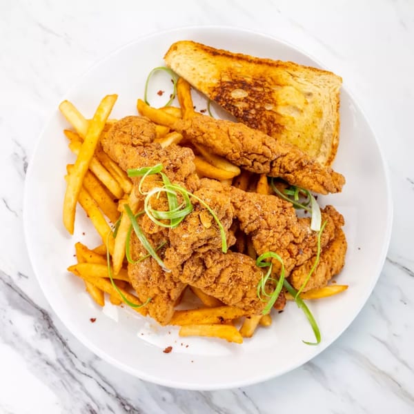 Crispy fried chicken tenders and golden french fries, garnished with green onions and a slice of toast.