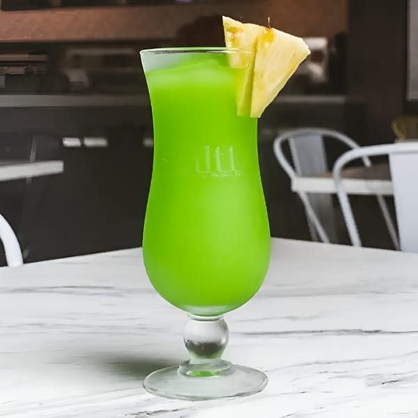 Vibrant green frozen drink in a tall glass, garnished with a pineapple wedge on a marble table.