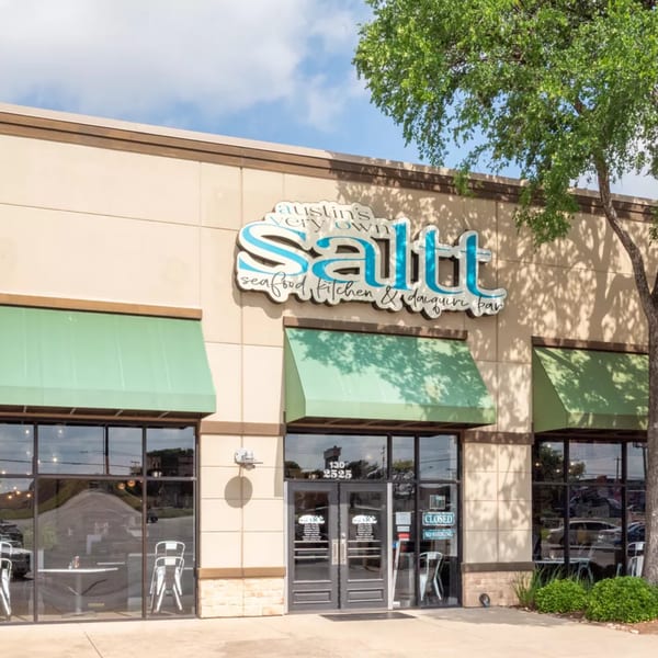 Exterior of Salt, a seafood kitchen and daiquiri bar, with green awnings and a tree.