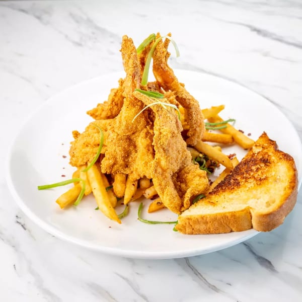 Golden fried shrimp and french fries with a slice of Texas toast on a white plate.