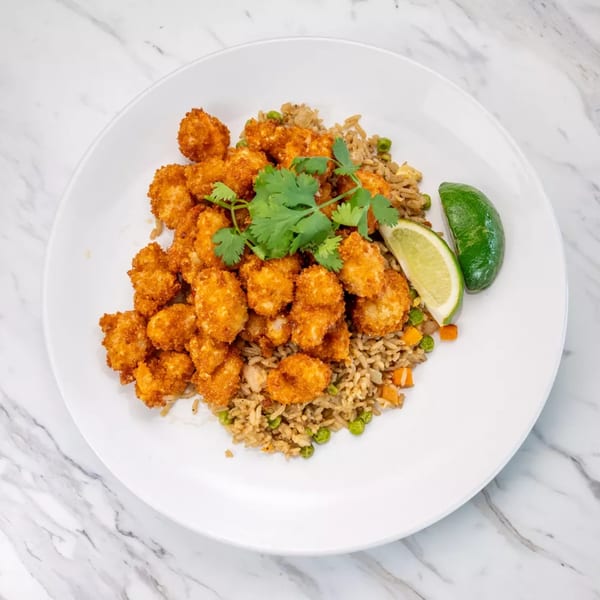 Crispy fried shrimp and vegetable fried rice, garnished with cilantro and lime wedges on a white plate.