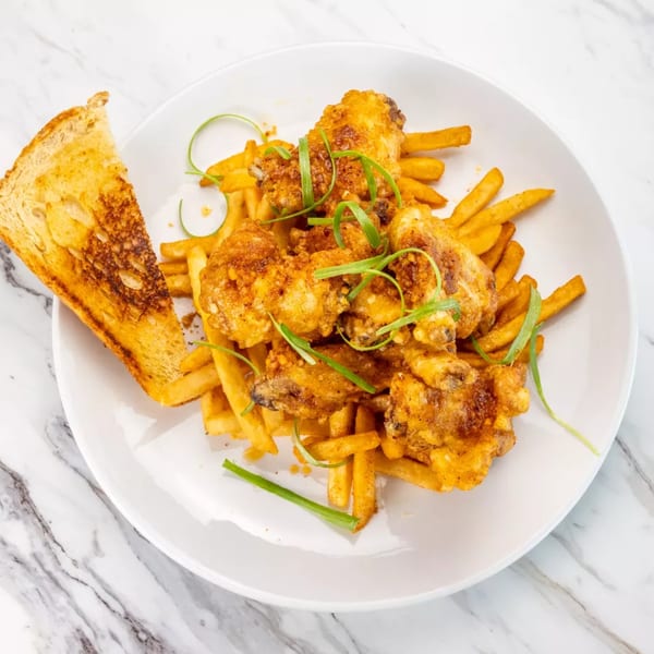 Crispy fried chicken wings and golden french fries garnished with green onions and a slice of toast.
